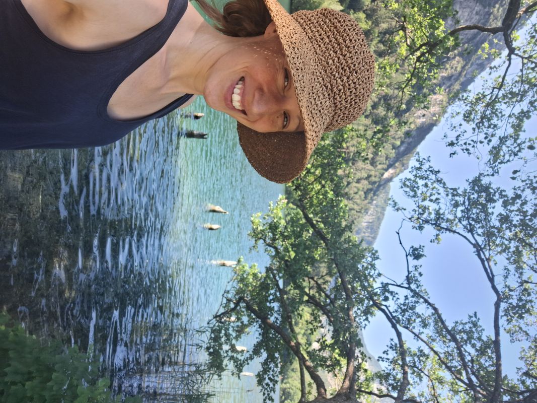 Malina lachend am See mit Strohhut, umgeben von Bergen und Natur
