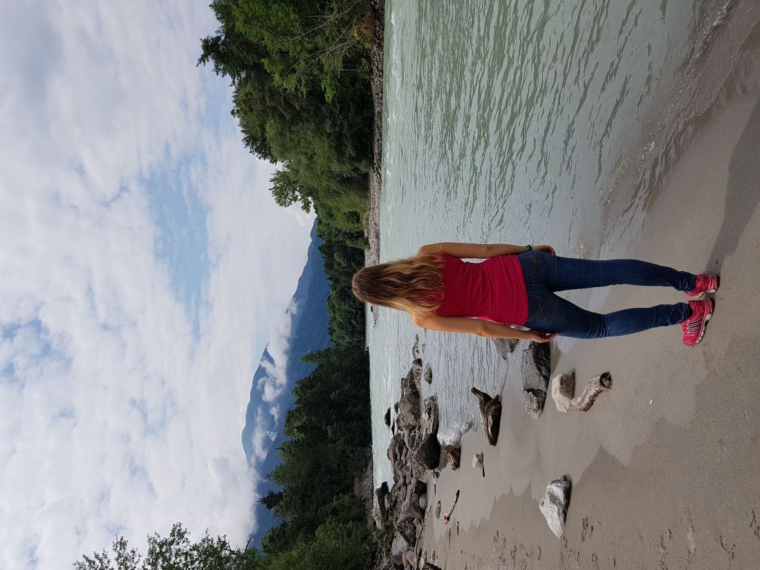 Malina steht am Ufer eines Flusses, Berge und Wald im Hintergrund